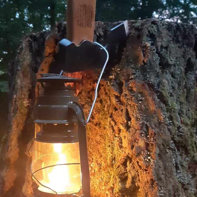 Eine überkopf in einem Baumstamm geschlagene Axt, an welcher eine Laterne mit einer Kerze hängt.